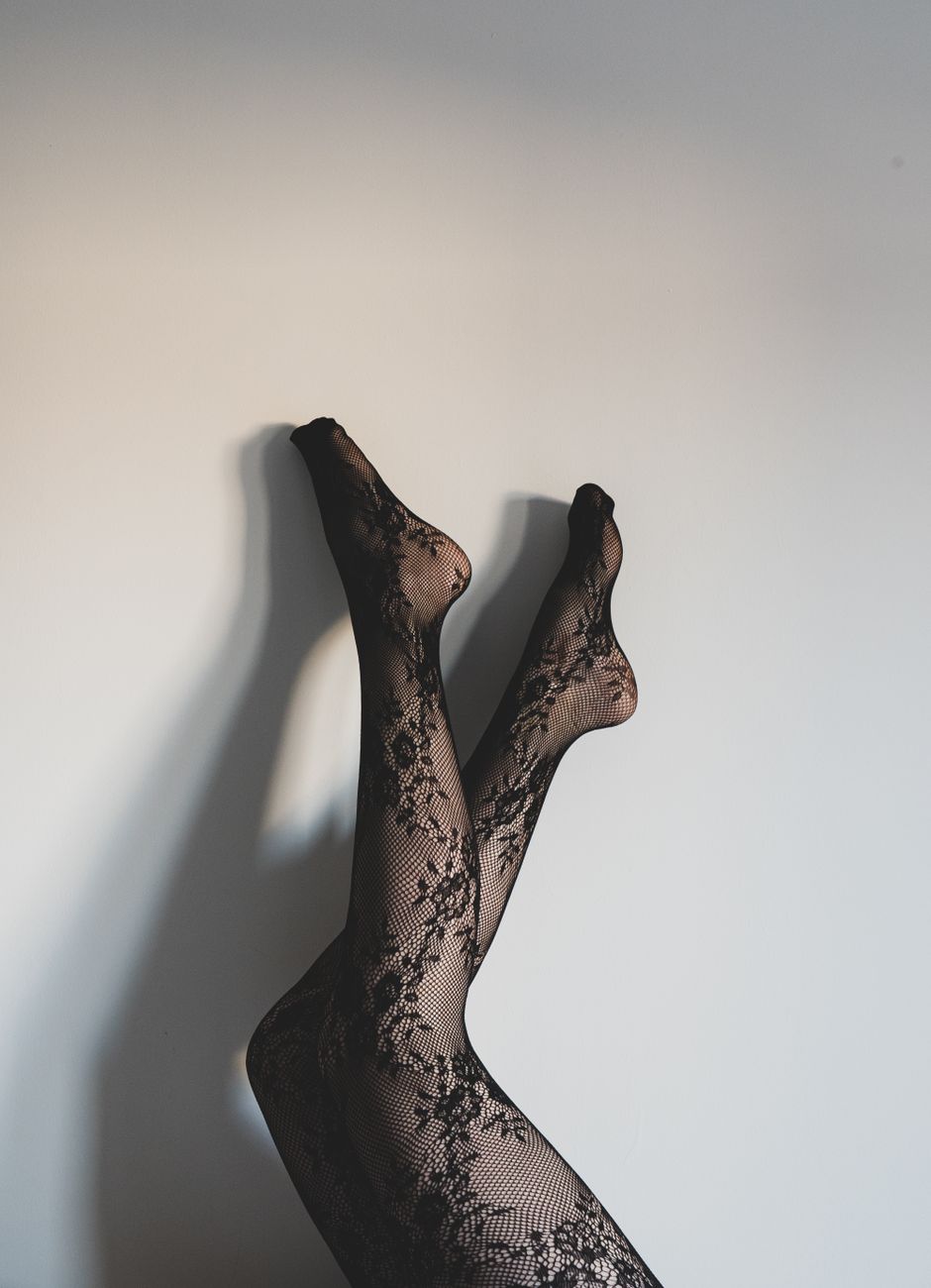 Artistic photo of female legs in lace stockings against a white wall.