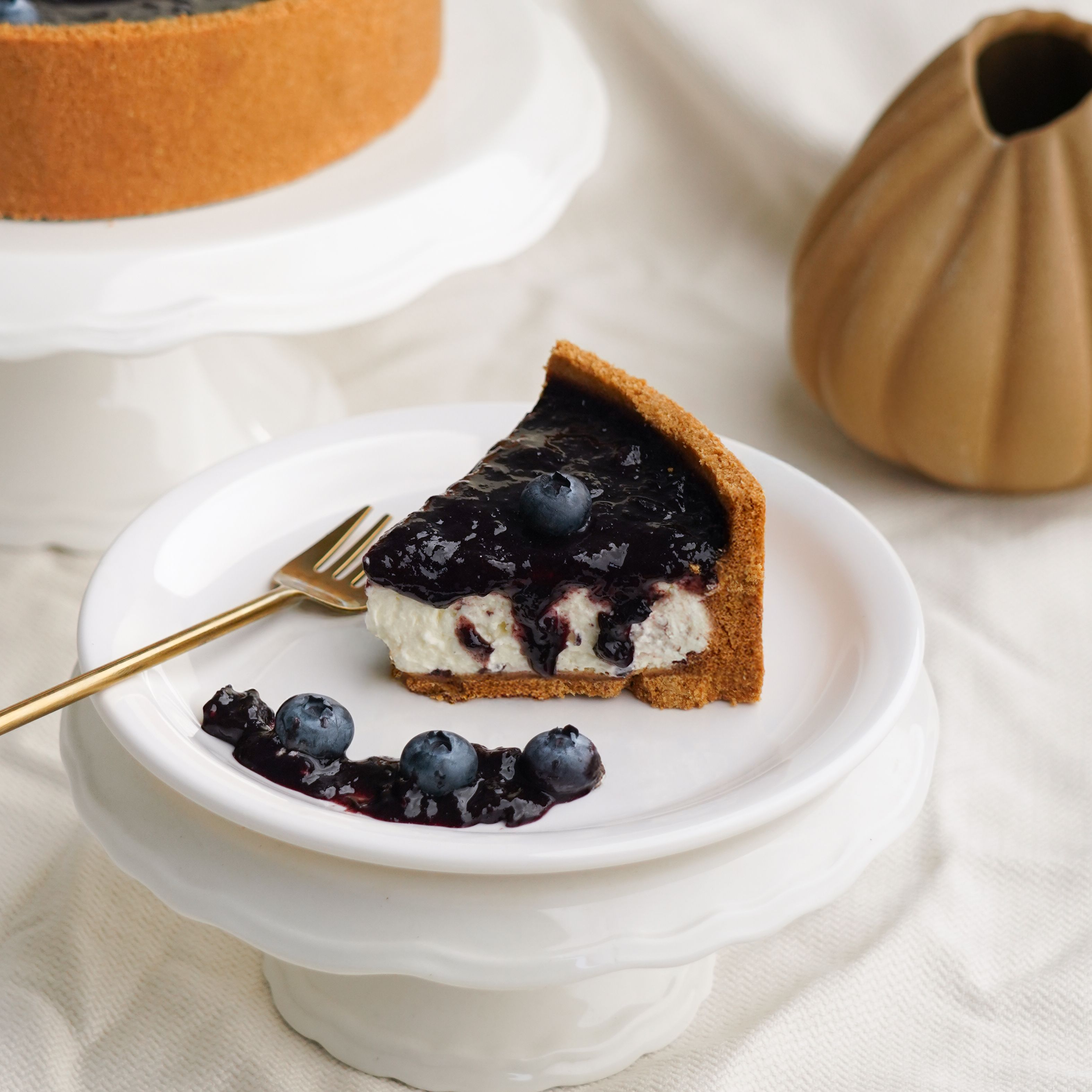 Delicious slice of blueberry cheesecake with fresh blueberries on a white plate, perfect for dessert presentations.