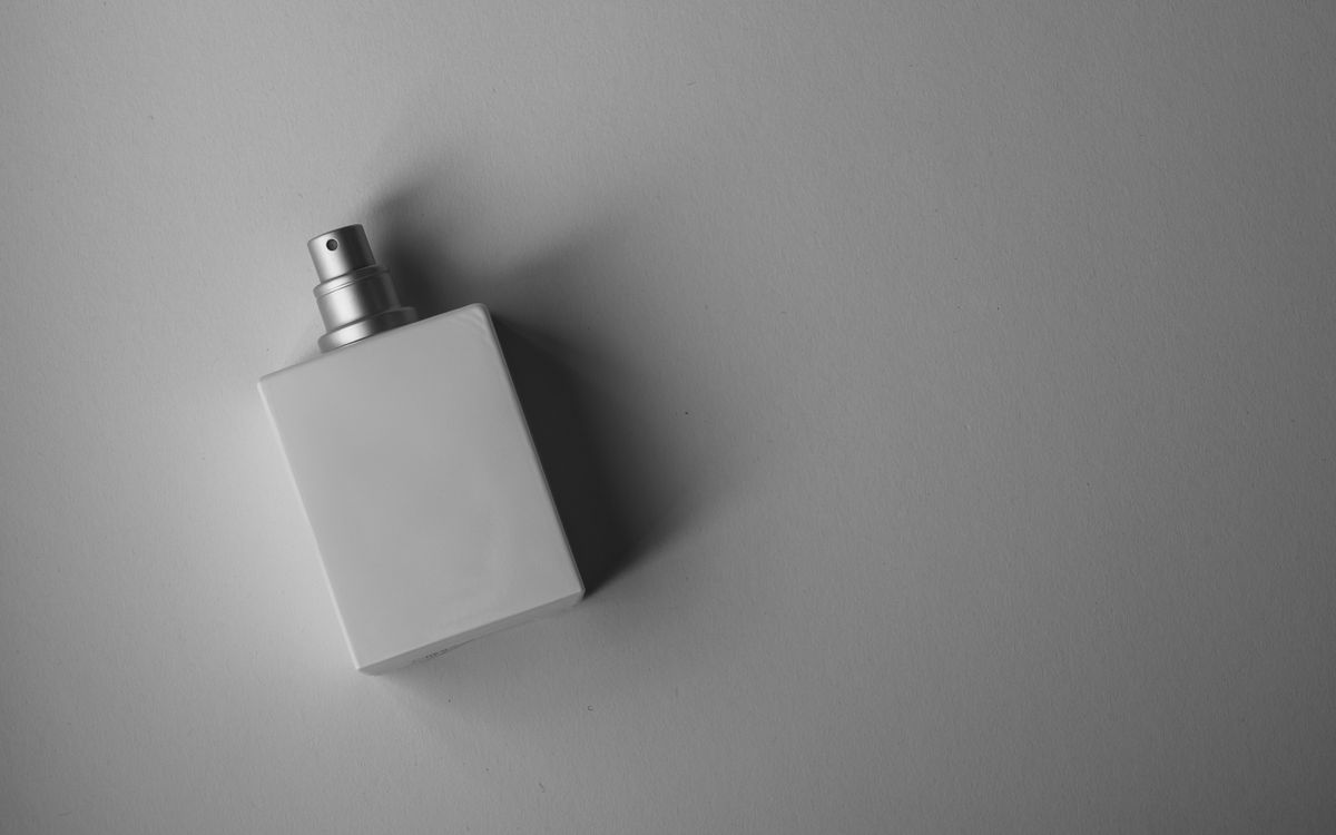 A sleek white perfume bottle photographed on a gray background with soft, muted lighting.