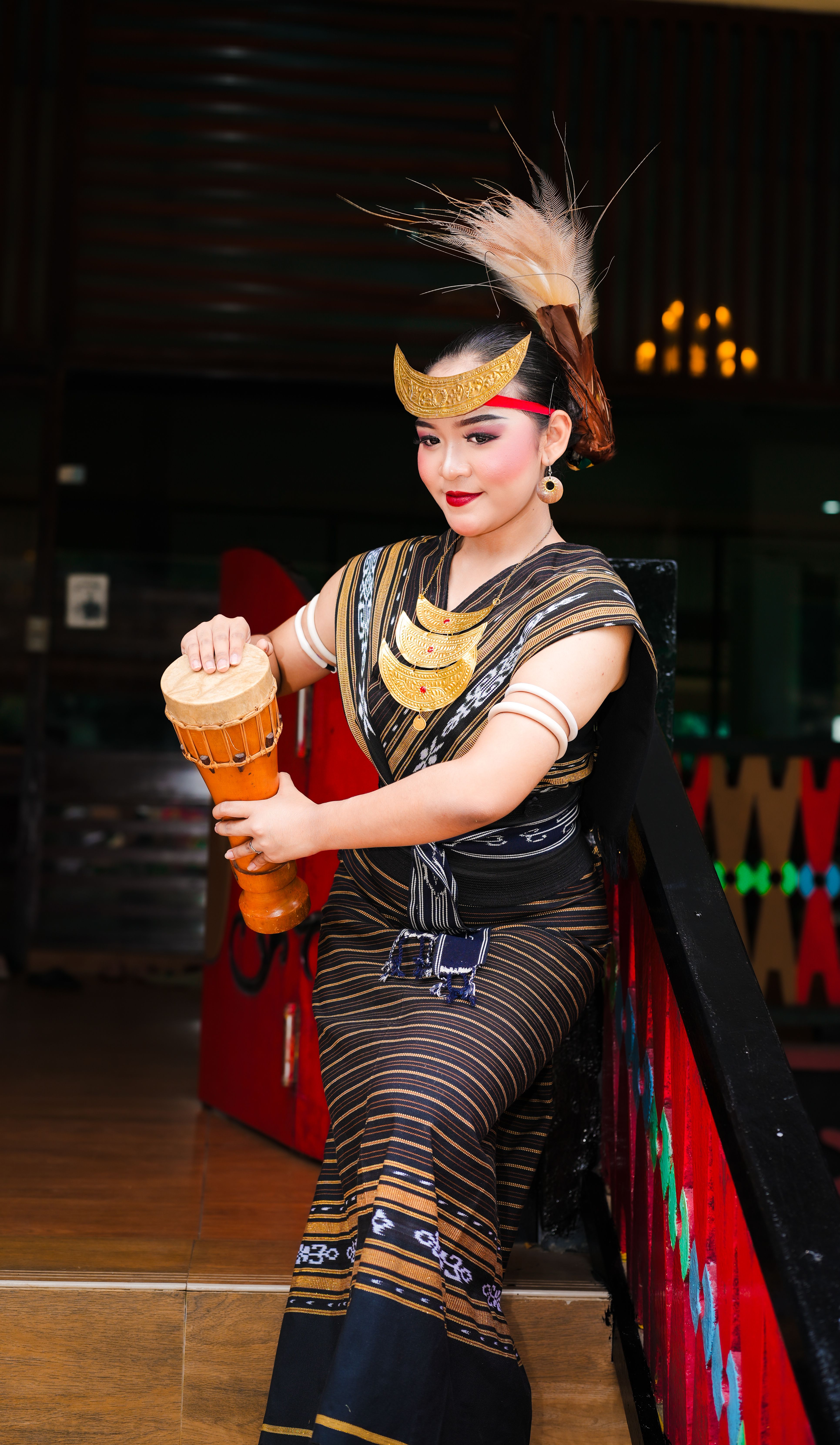 A woman in traditional Indonesian attire playing a drum in Jakarta. Captured indoors with vibrant, artistic style.