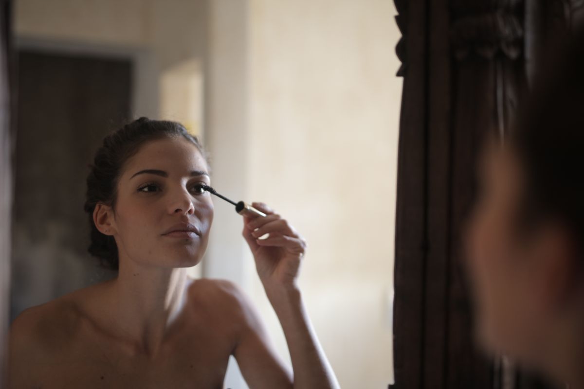 Mulher aplicando máscara de cílios diante do espelho
