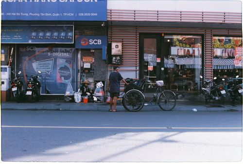 Free A lively street scene in a Vietnamese city featuring a cyclist and local shops. Stock Photo