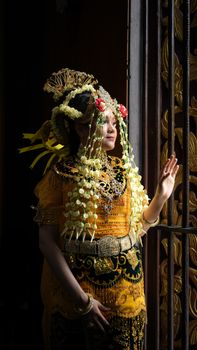 Woman in traditional Indonesian bridal attire gazing out a window, adorned with intricate jewelry. - Fotografer Sidoarjo