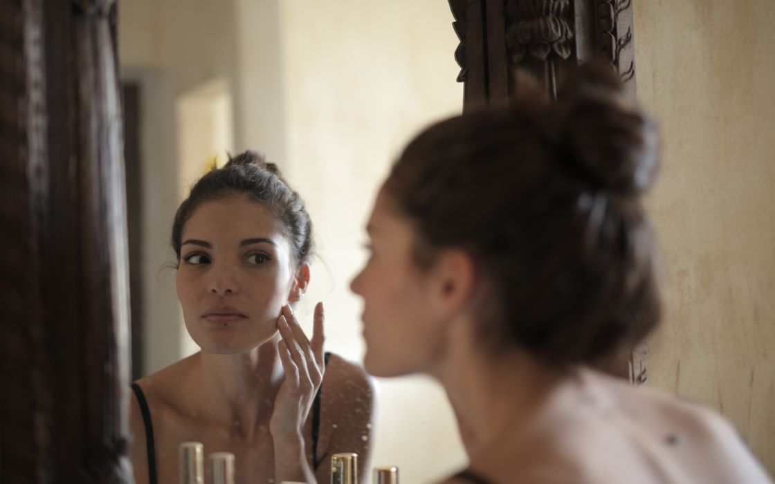 Woman touching her cheek while studying her reflection in a mirror