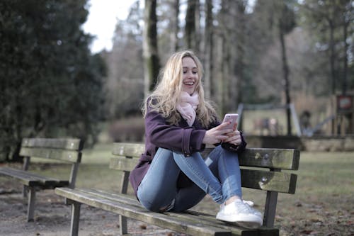 Woman in Purple Jacket and Blue Denim Jeans Sitting on Brown Wooden Bench