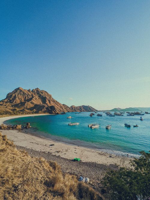 Free A stunning view of Padar Island showcasing its blue waters, sandy beach, and boats under clear skies. Stock Photo