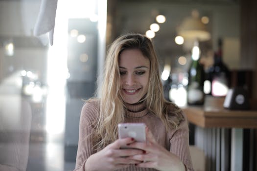 A joyful woman with blonde hair texting on her smartphone in a cozy cafe.