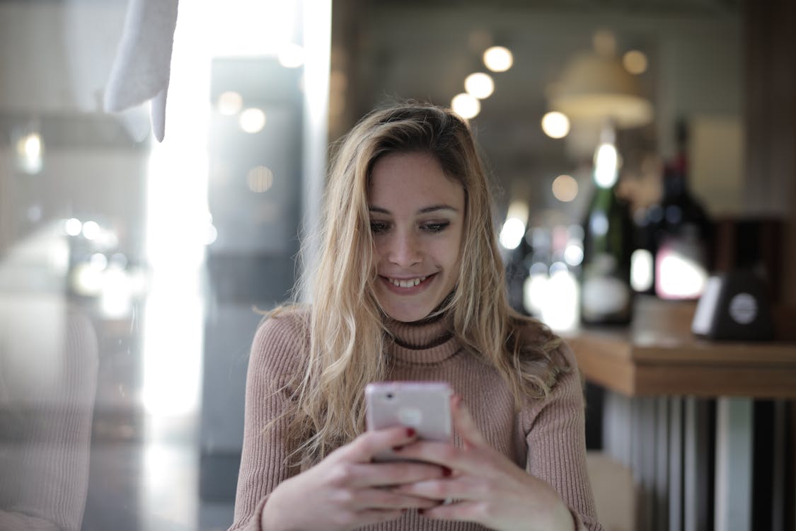 Free Woman in Brown Knit Sweater Holding White Smartphone Stock Photo