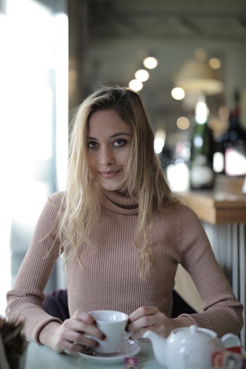 Free Blonde woman sipping coffee in a cozy cafe with warm lighting. Stock Photo