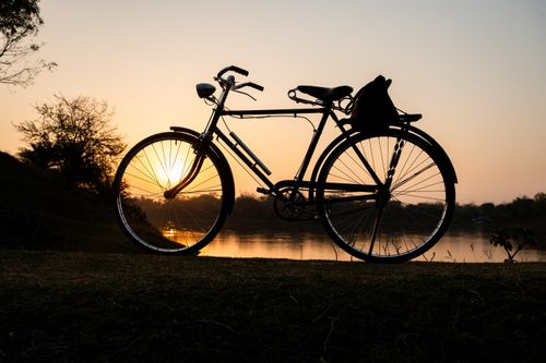 Free Silhouette of an old bicycle by a river during sunset, creating a nostalgic and serene scene. Stock Photo