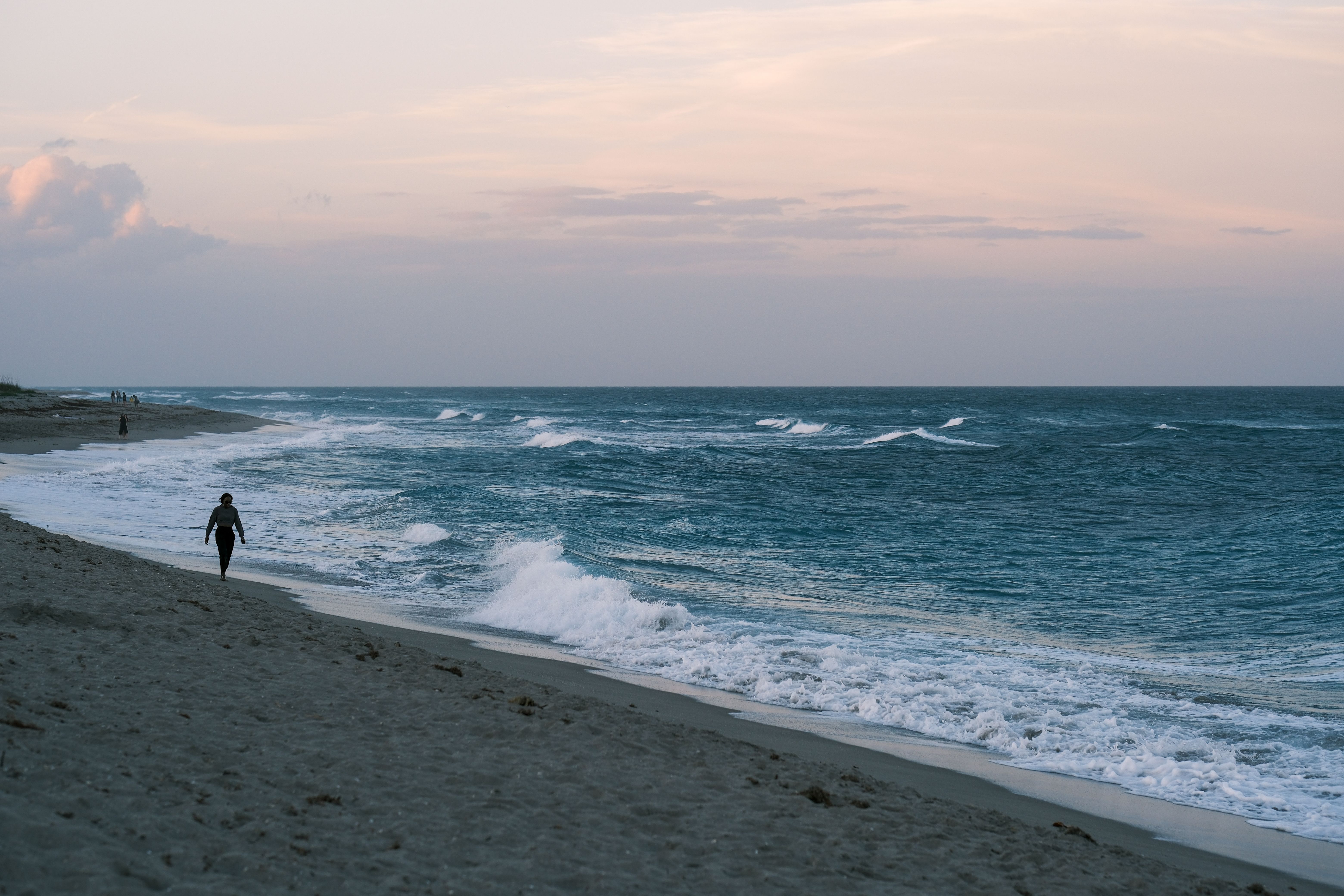 A person walks along a tranquil beach at sunset, enjoying the soothing sound of waves.