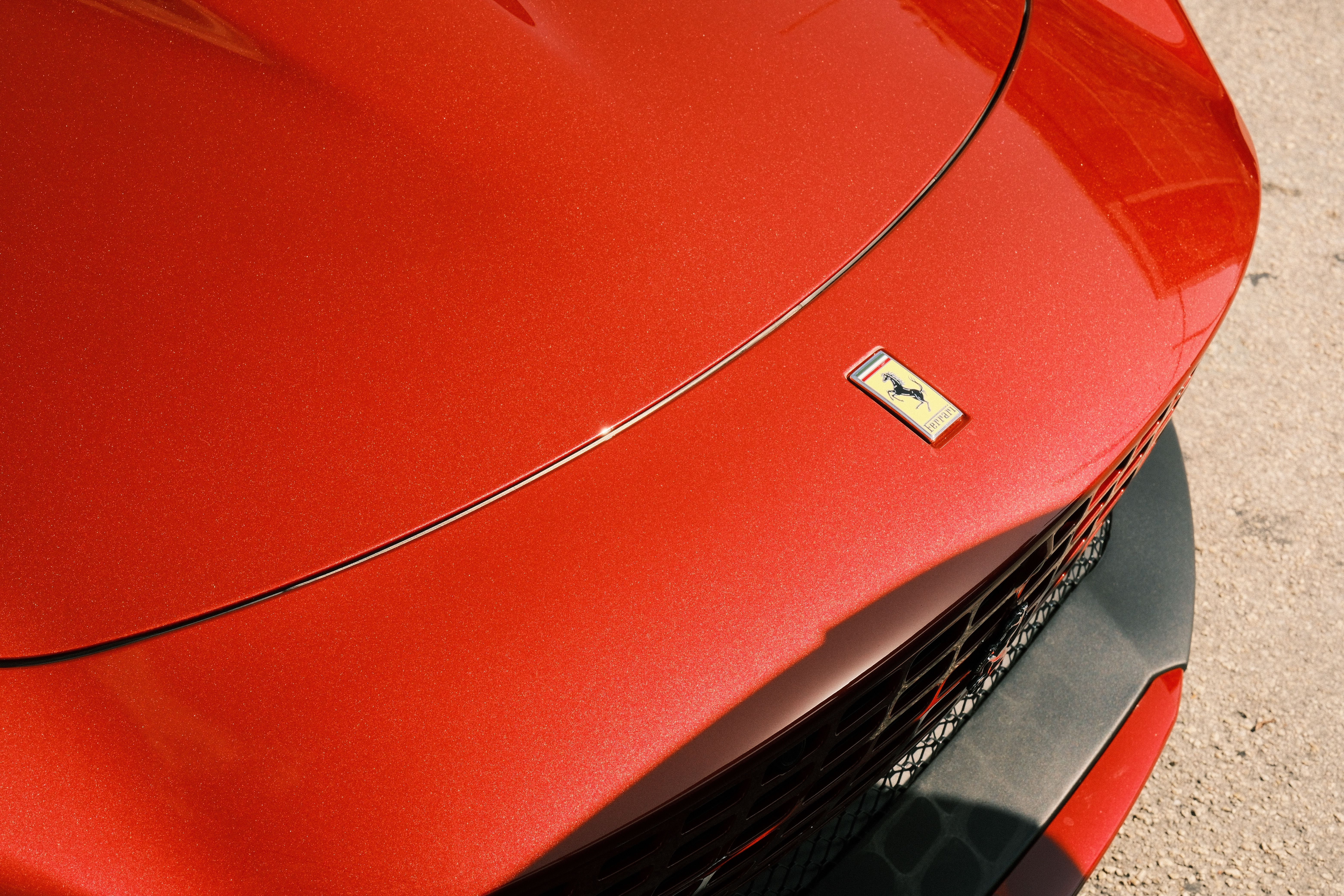 Close-up view of a luxurious red sports car hood featuring a sleek design and emblem.