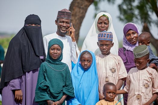 A diverse family group in traditional attire posing outdoors with warm smiles.