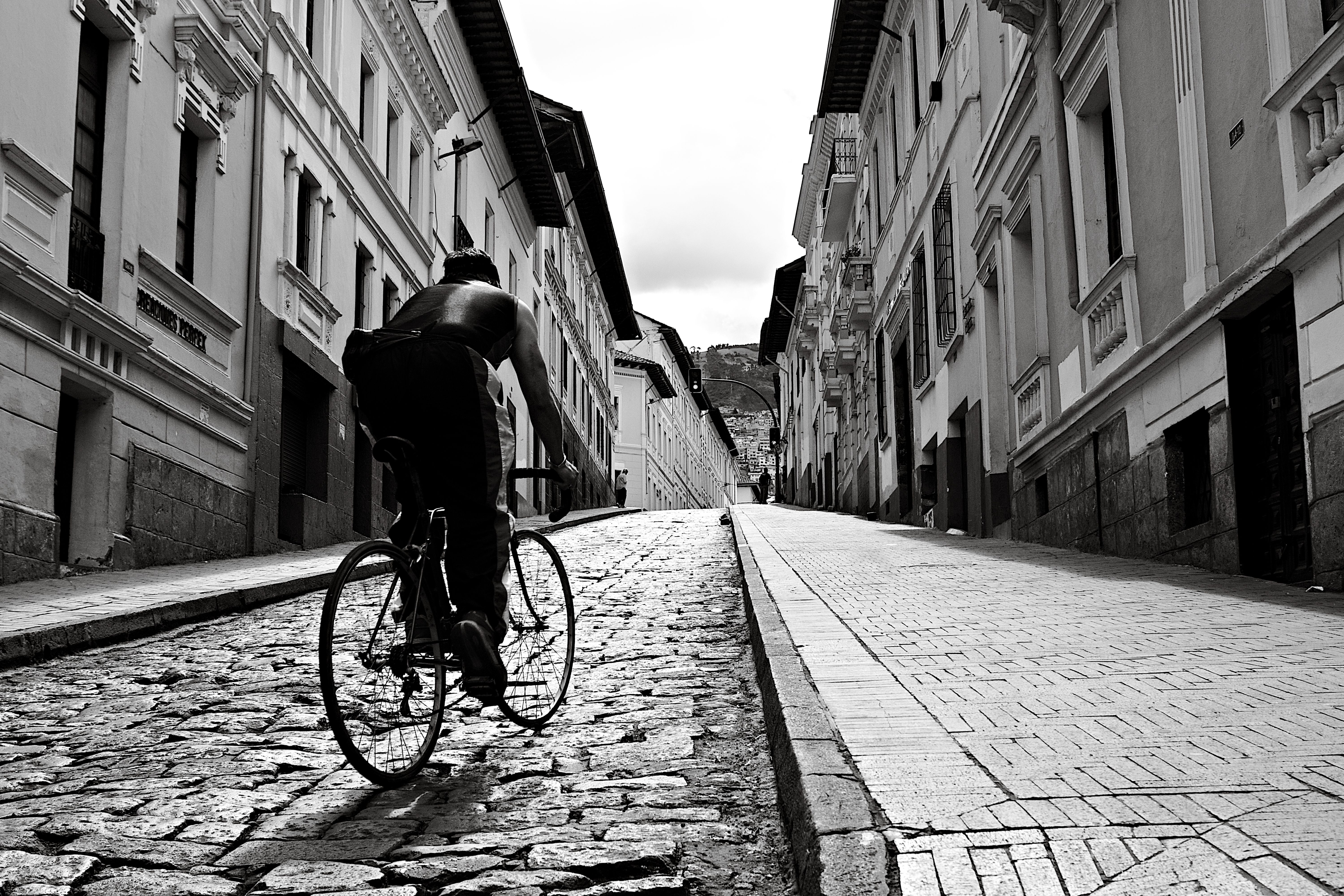Black and white image of a cyclist navigating the cobblestone streets in historic area of Quito, Ecuador.