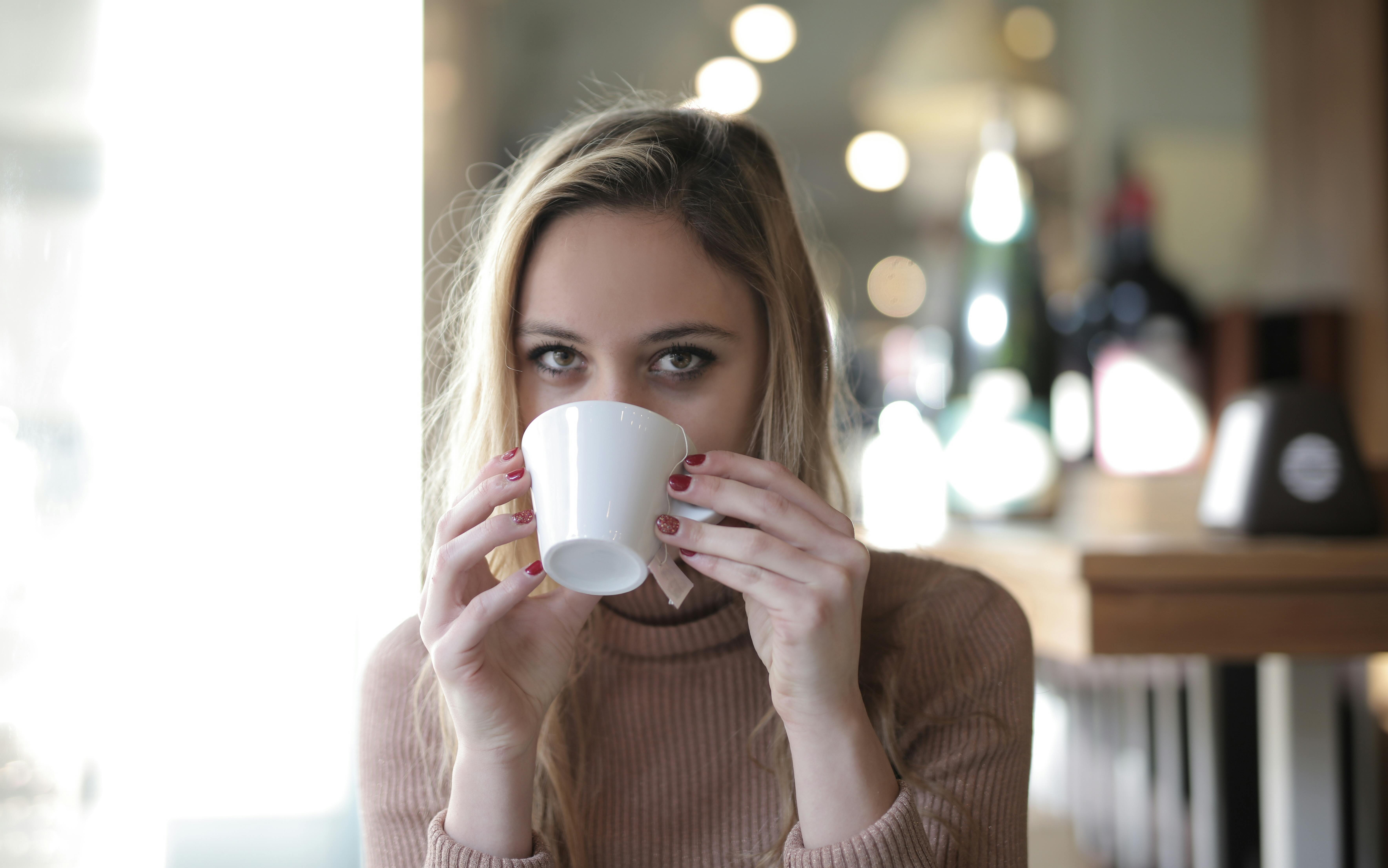 woman in sweater holding white ceramic mug