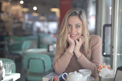 Woman in Brown Sweater Sitting by the Table