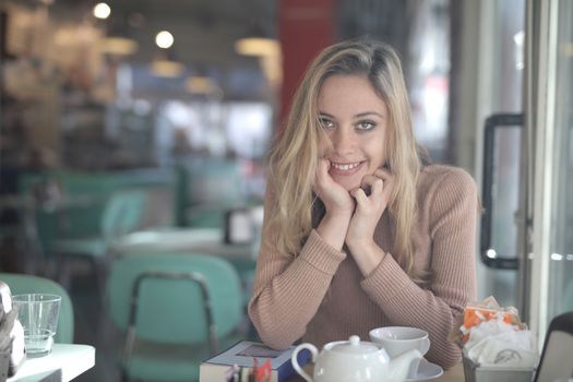 Blonde woman smiling at a table in a cozy cafe with a relaxed vibe.