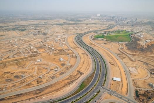 Wide aerial view of a developing desert highway with surrounding construction sites.