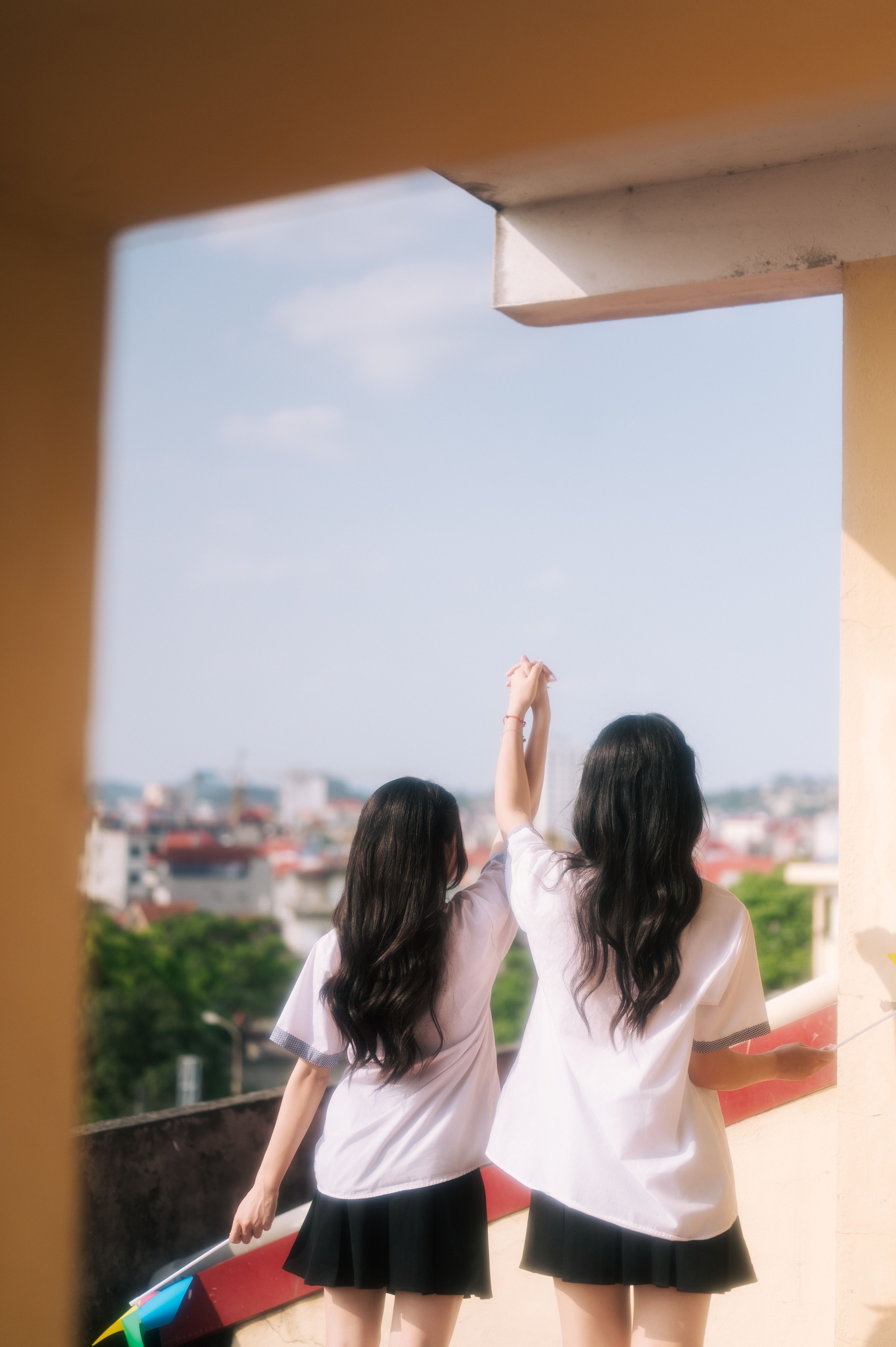 Two teen girls happily hold hands on a sunny rooftop in Lạng Sơn, Việt Nam.