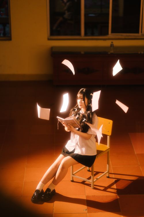 Free A girl in a classroom with papers floating around, creating a whimsical study atmosphere. Stock Photo