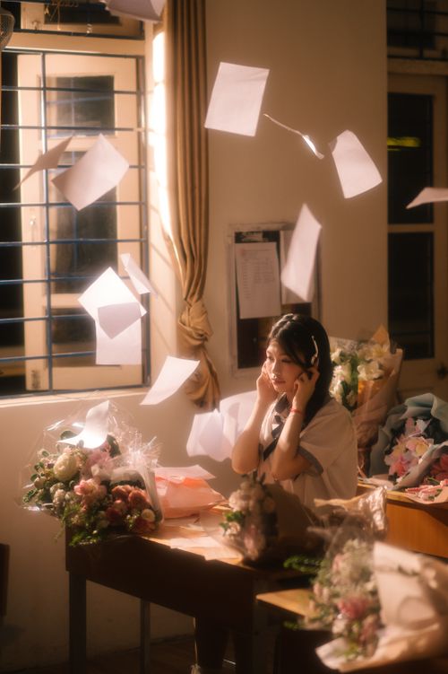 Free A dreamy scene of a girl daydreaming with flying papers and flowers in a cozy room. Stock Photo