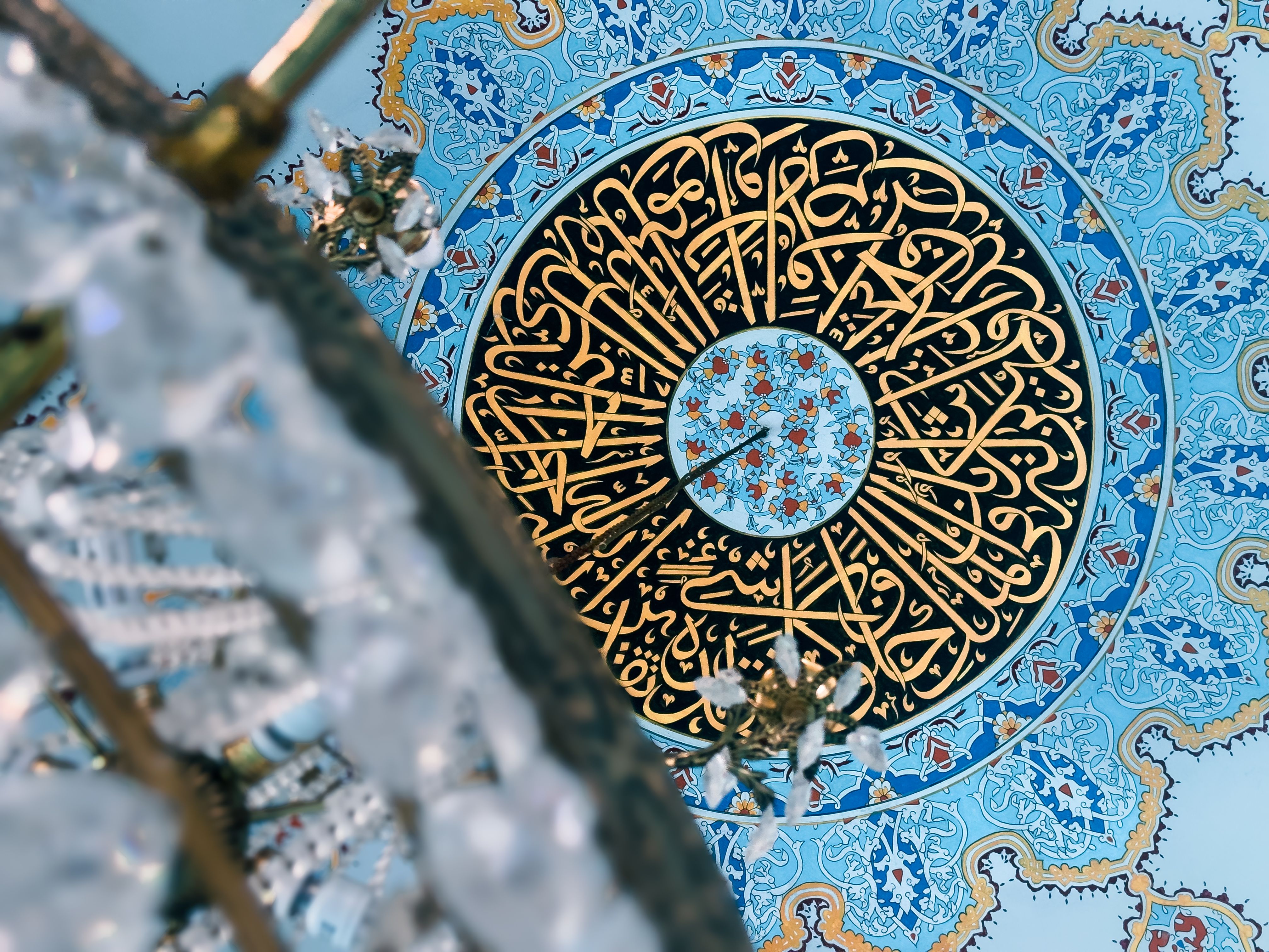 Detailed view of a mosque ceiling featuring elaborate Arabic calligraphy and blue geometric patterns.