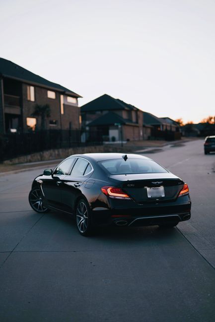 A sleek black luxury sedan parked on a quiet residential street during twilight.