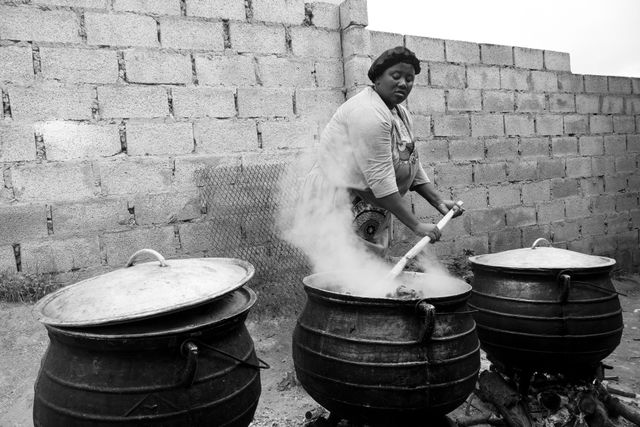 A woman cooking traditional South African stew in large pots outdoors.