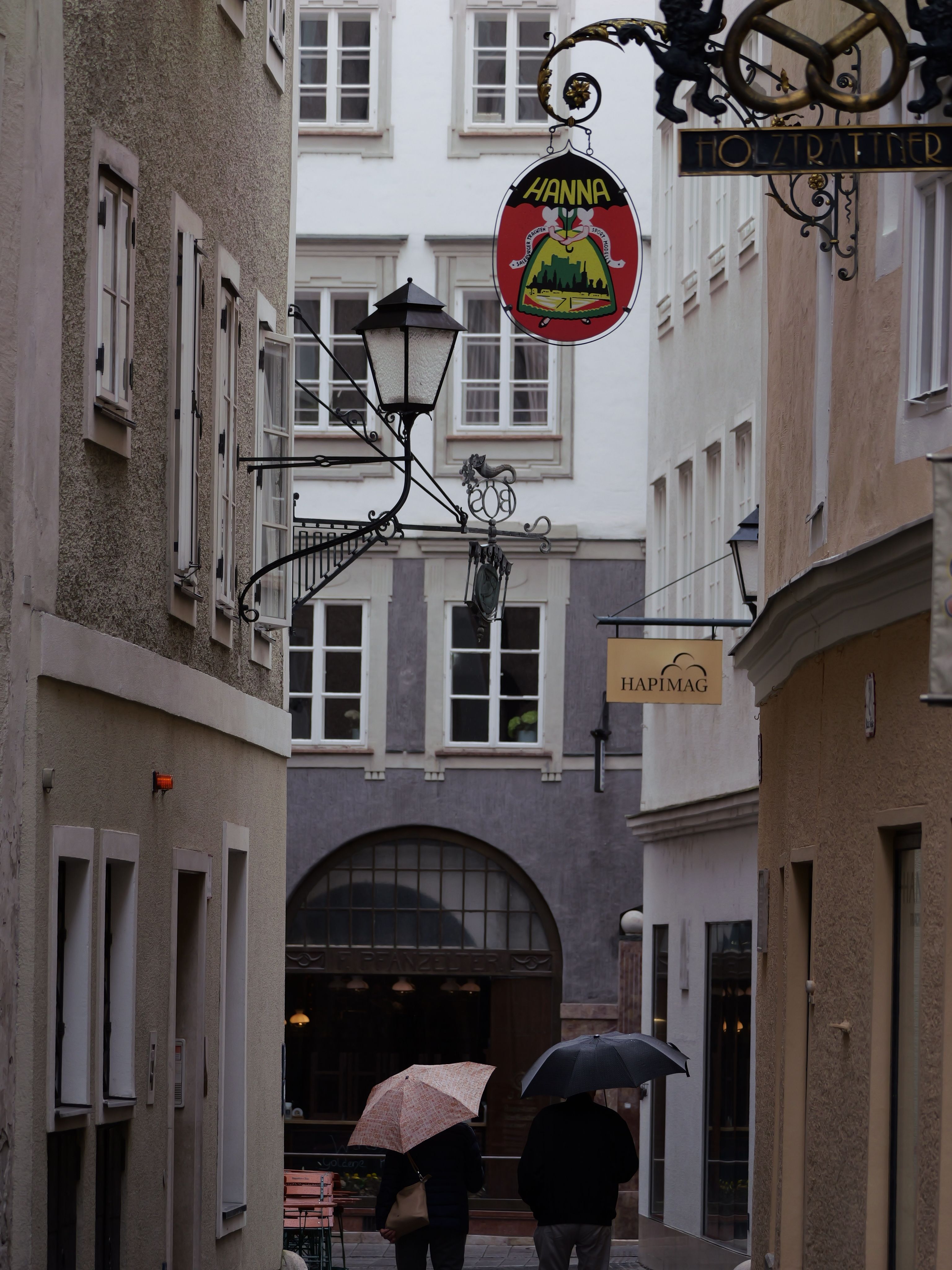 Charming rainy alley in Salzburg, Austria with umbrellas and vintage signs.