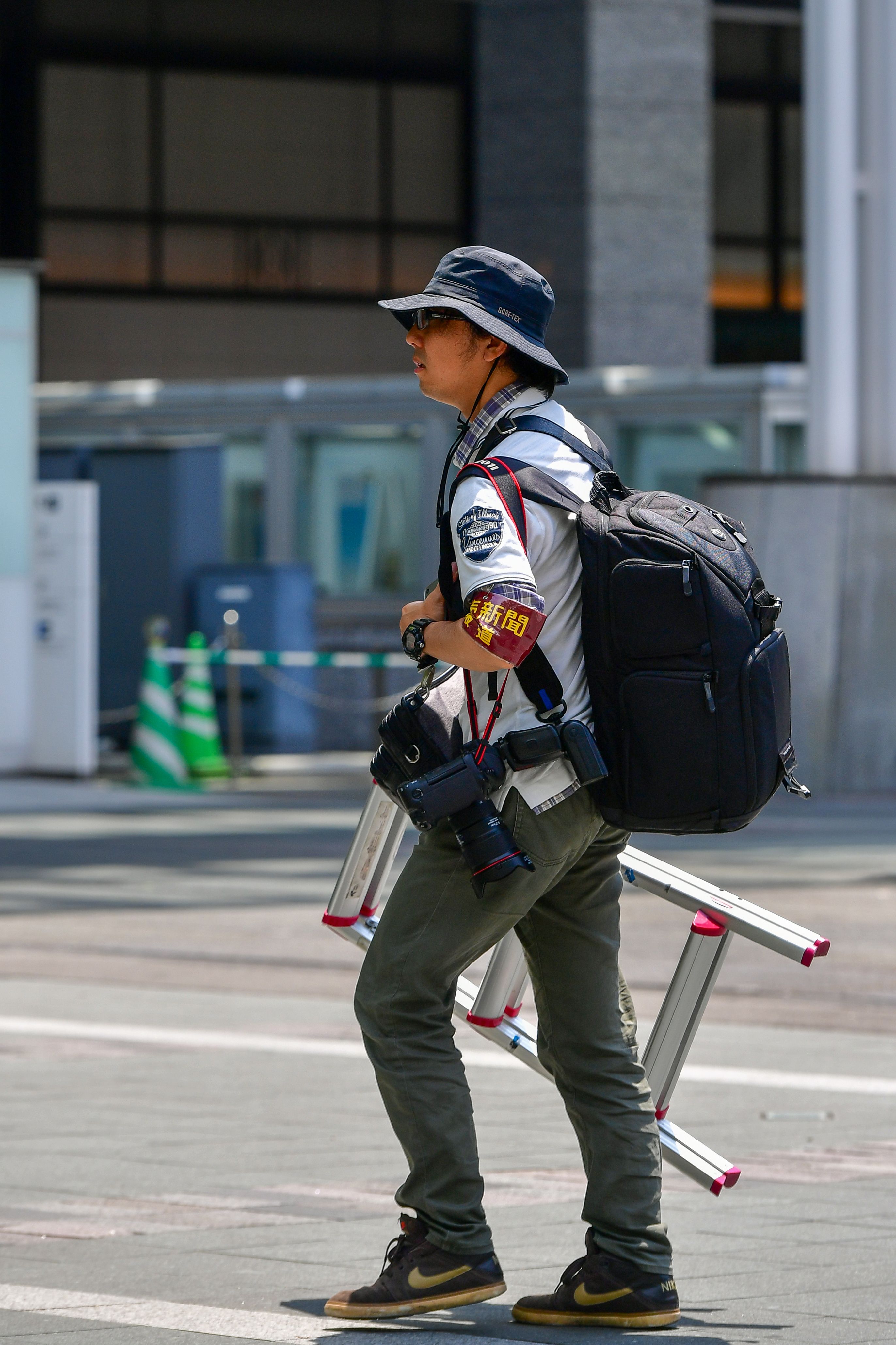 Street photographer in Tokyo carrying a ladder and camera gear on a sunny day.