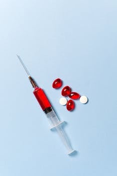 Syringe with red liquid and pills on a blue backdrop symbolizing medical treatment.