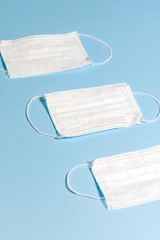 柔和的蓝色背景上排列着三个白色口罩，象征着健康保护