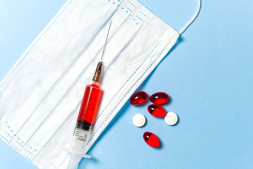 Free A syringe, face mask, and pills on a blue surface, symbolizing medical treatment. Stock Photo