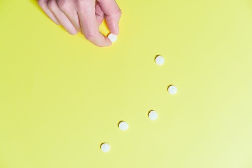 Foto Der Hand Der Person, Die Weiße Pille Gegen Gelben Hintergrund Hält