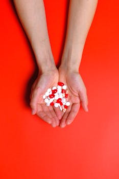 Close-up of hands holding multiple red and white pills on a vibrant red background.