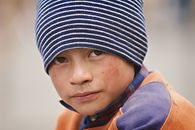 A close-up portrait of a young boy wearing a striped beanie, looking thoughtfully into the camera.