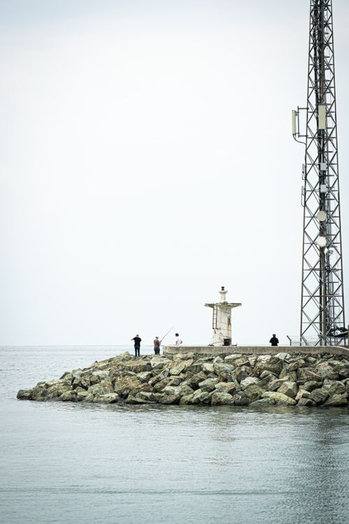 Free A serene scene of a lighthouse and people fishing on a rocky coastline in Yalova, Türkiye. Stock Photo