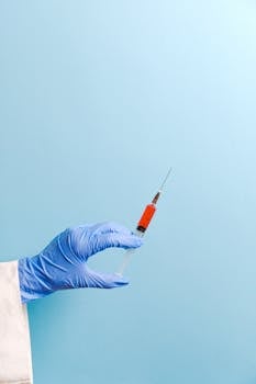 Gloved hand holding a syringe on a light blue background, representing medical procedures.