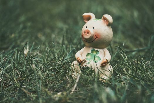 Charming ceramic pig figurine with shamrock, symbolizing luck, nestled in lush green grass.