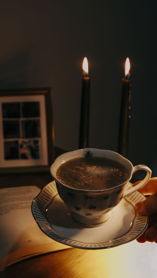 Free A warm, intimate evening setting with a cup of tea, candlelight, and a book. Stock Photo