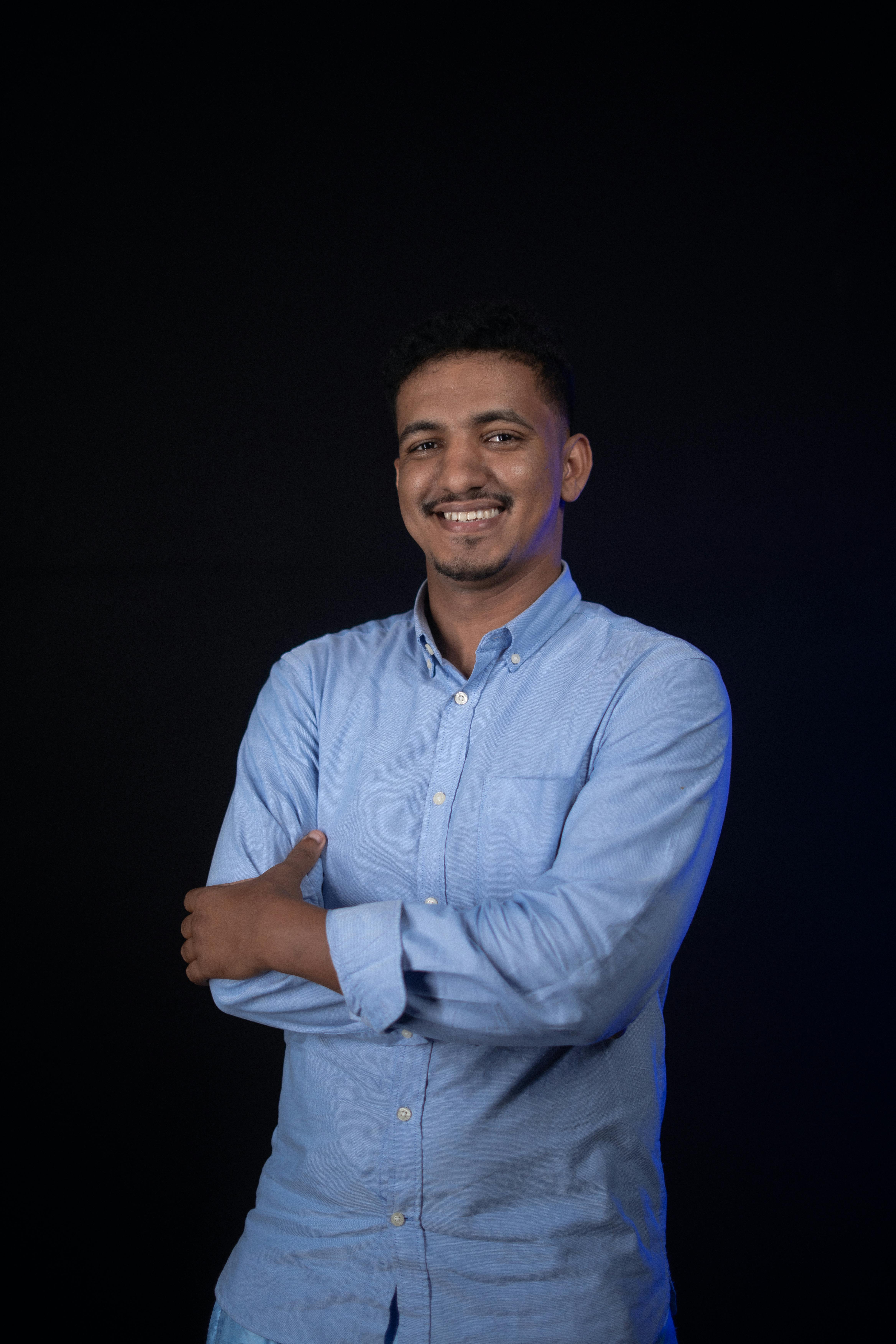 A cheerful man in a blue shirt posing against a dark background.
