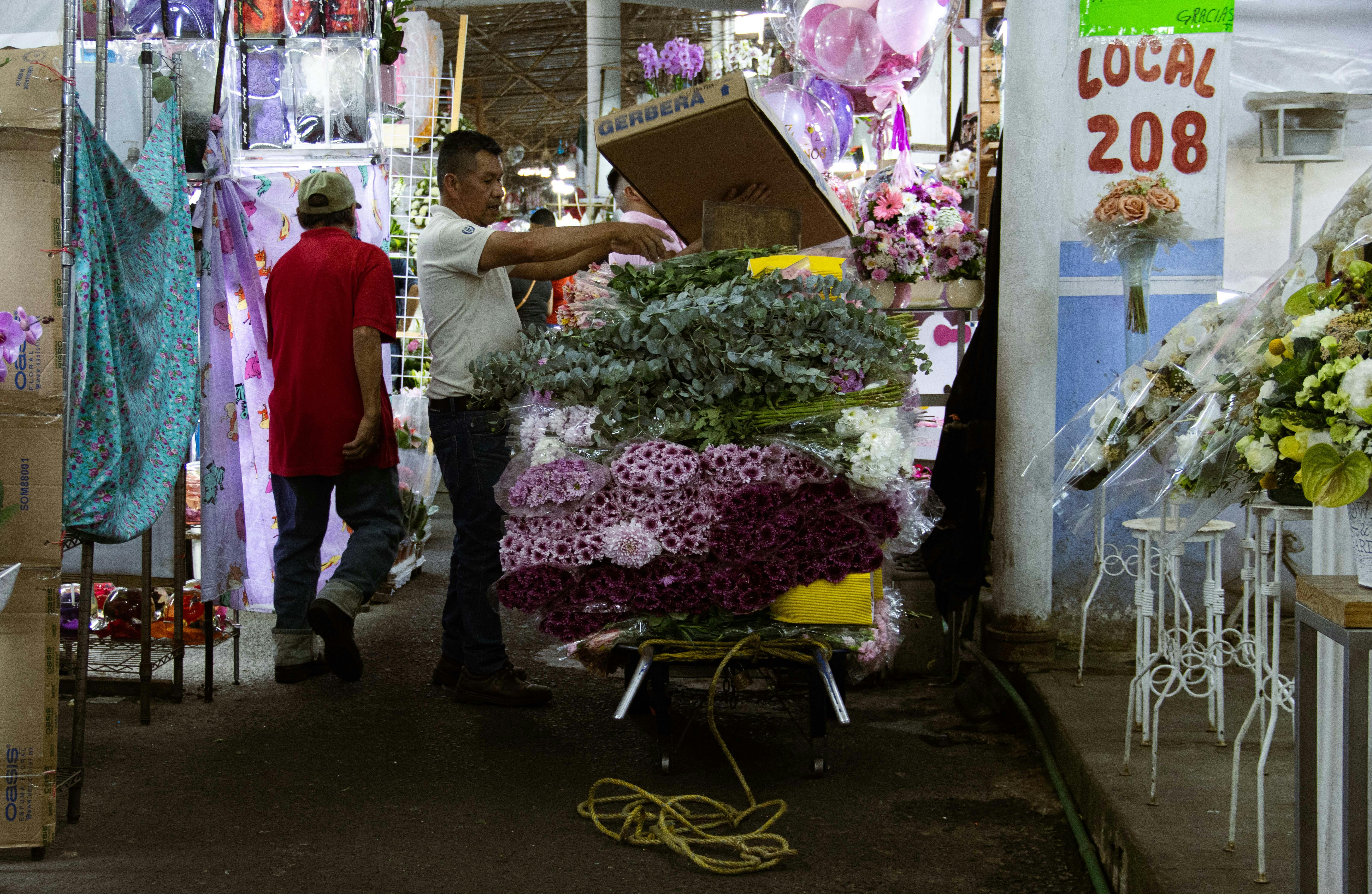 Two men arranging flowers at a vibrant indoor market stall, showcasing colorful bouquets.