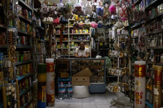 A vibrant small shop full of diverse products and a shopkeeper behind the counter.