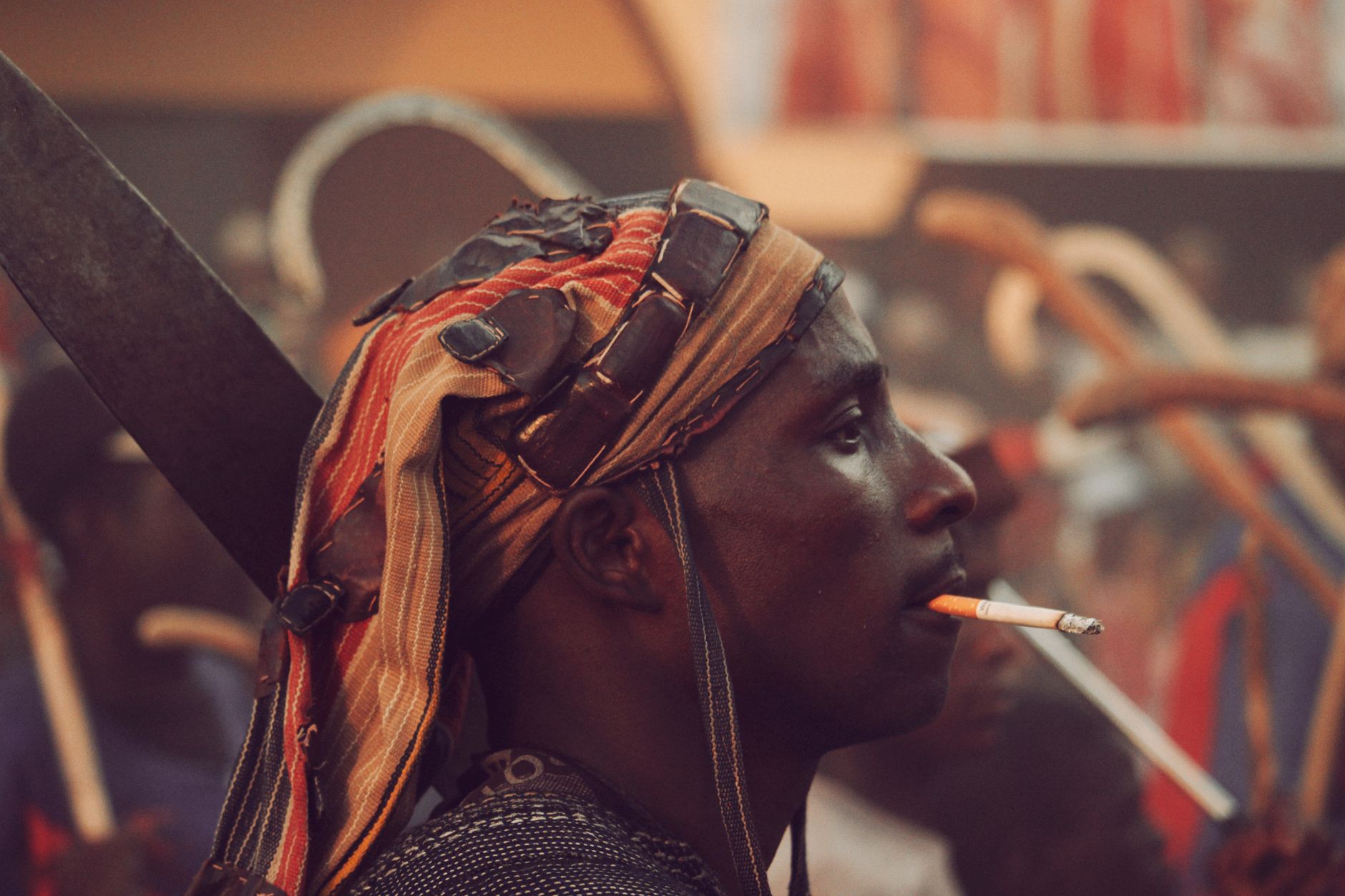 A Nigerian man in cultural attire attends a traditional festival, holding a smoking pipe.