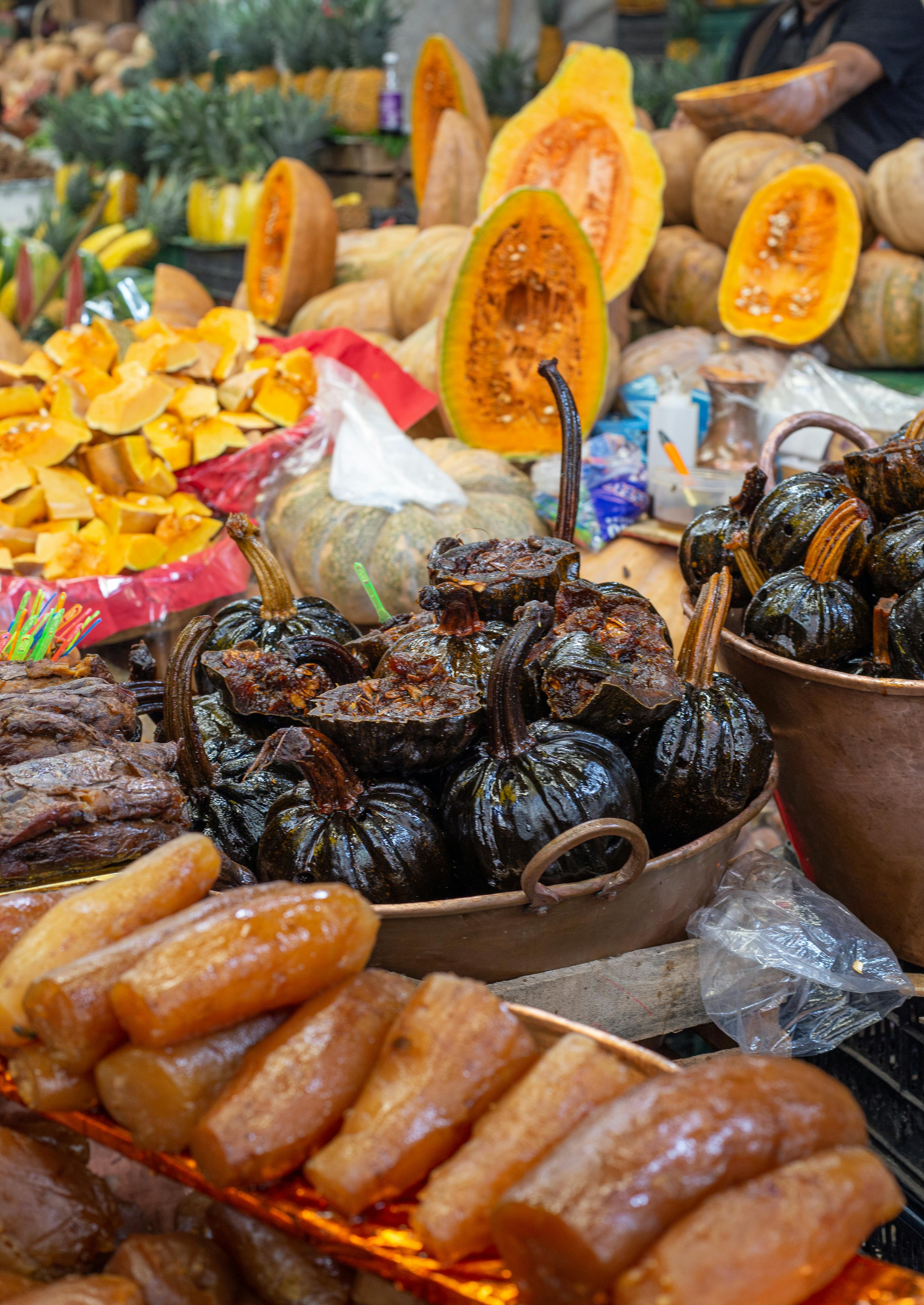 Colorful display of traditional Mexican sweets and pumpkins at a bustling market stand.