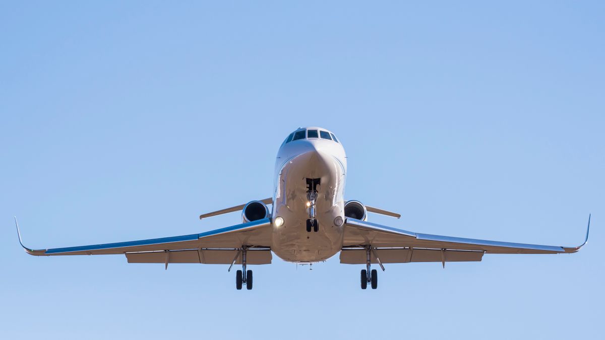 Front view of a private jet landing with extended gear against a clear blue sky