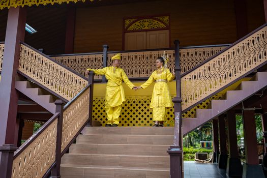 Couple in vibrant yellow traditional attire pose on decorative staircase outdoors.