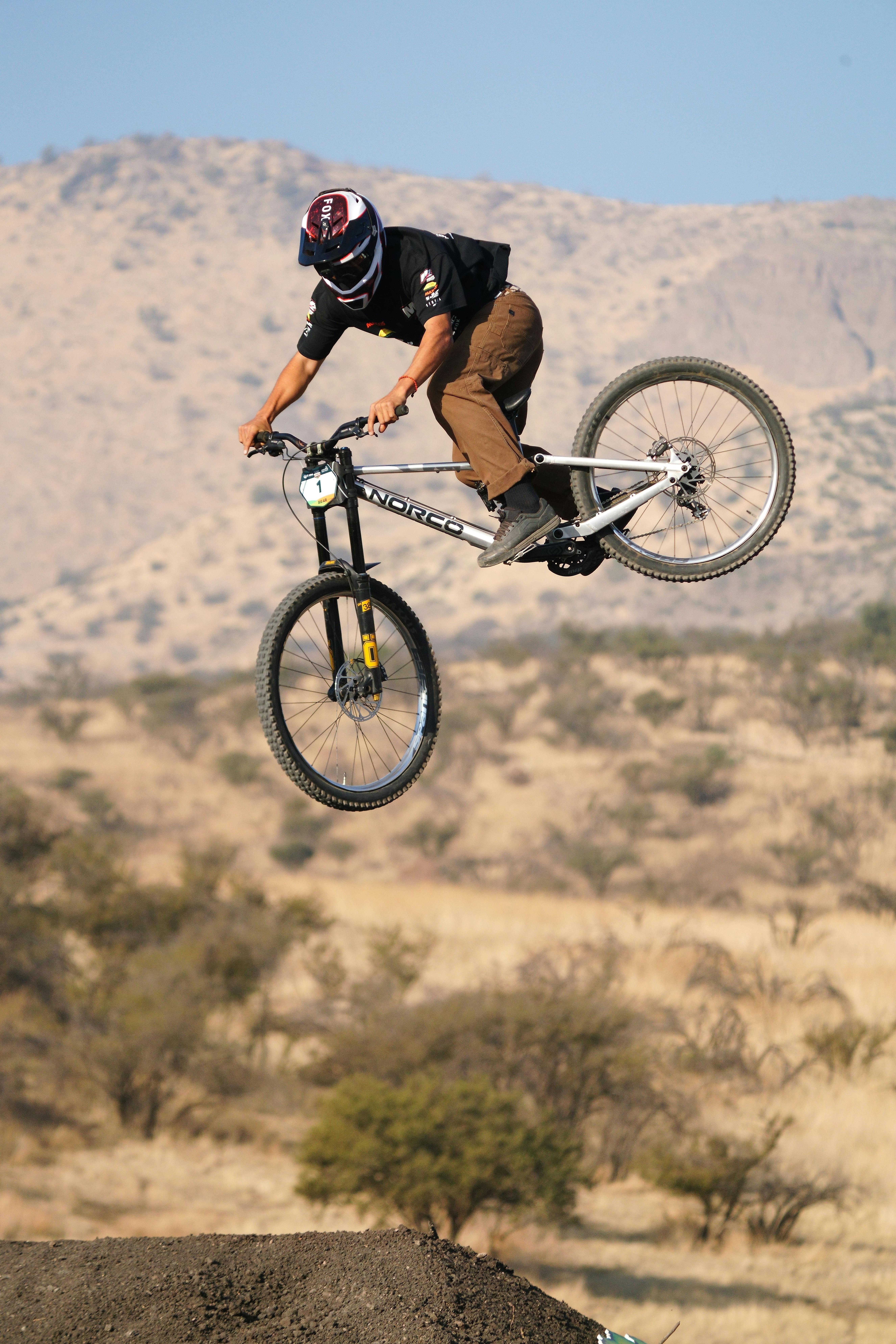 A mountain biker executes an aerial jump against a desert backdrop during daylight.