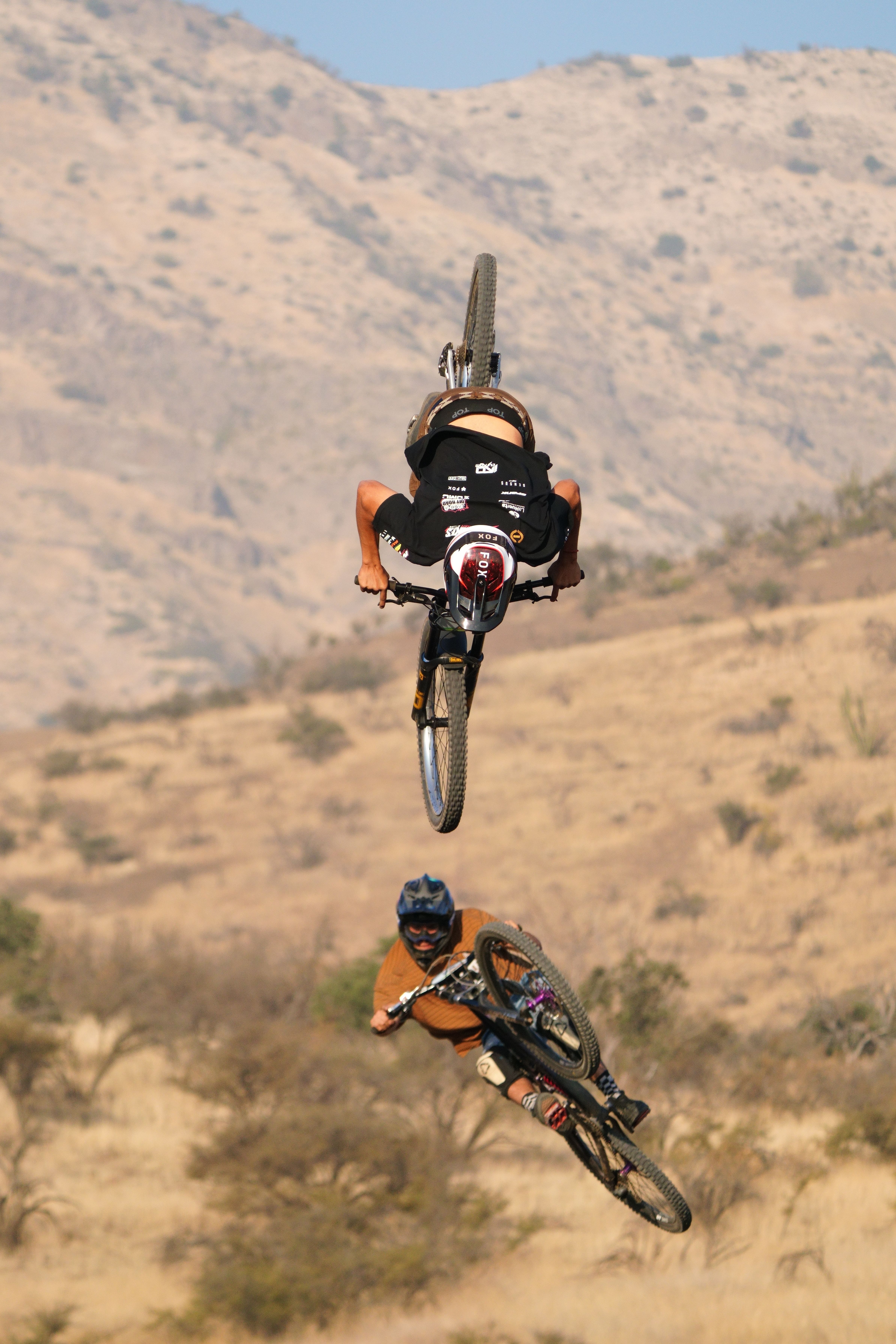 Two mountain bikers performing stunts in a rugged desert setting.