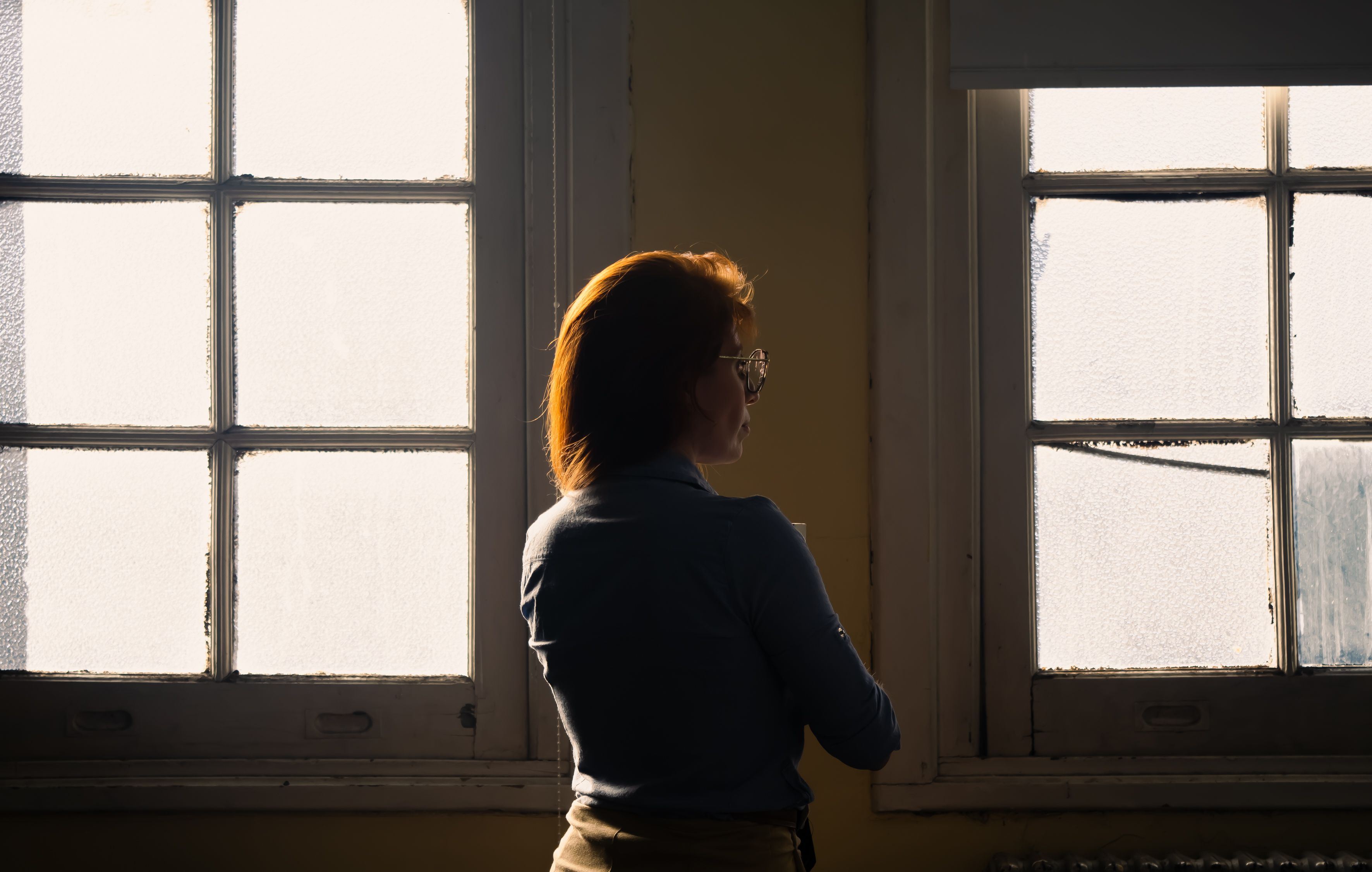 A thoughtful woman stands silhouetted against a frosted vintage window, evoking contemplation and solitude.